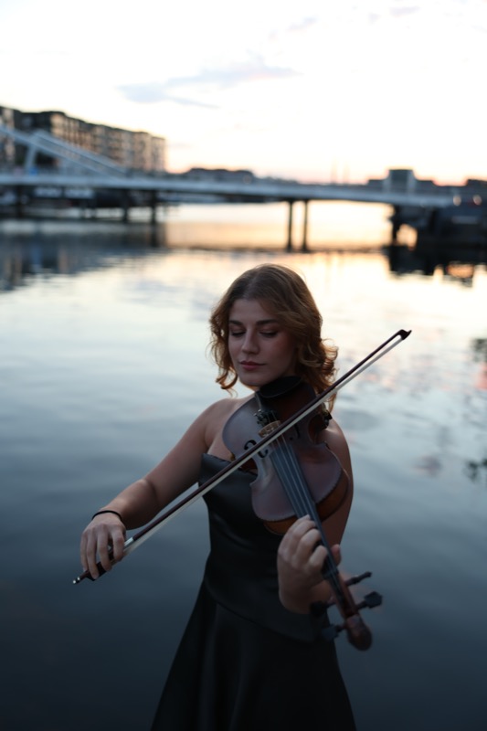 Violinspil ved havnen i solnedgang